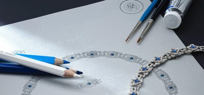 Close-up of jewelry design sketch with blue and white pencils, loose gemstones, and a silver necklace with blue stones. image