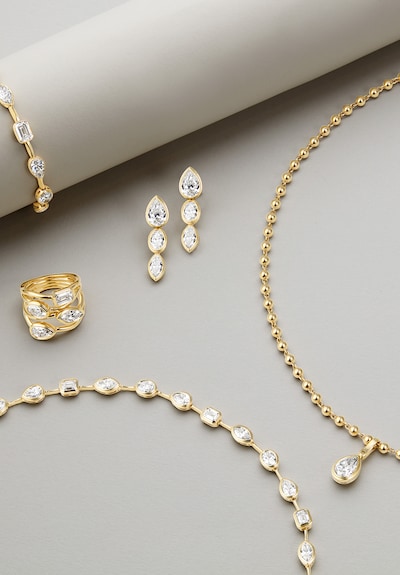 Close-up of bespoke gold jewellery for Kate Kane, with diamond earrings, ring, bracelet, and pendant necklace arranged on a grey surface image